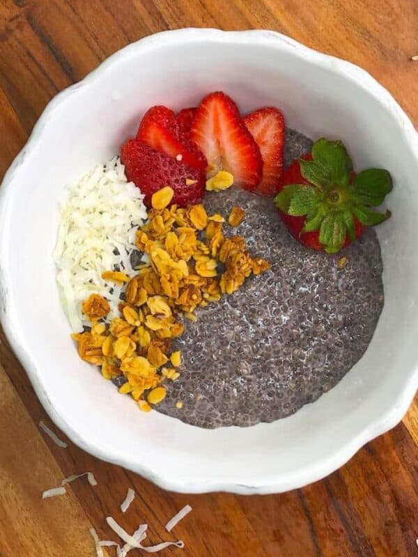 Top shot of chia seed pudding topped with sliced strawberries, granola, and shredded coconut in a white bowl on a wooden board.