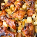 A serving plate with baked BBQ chicken drumsticks, garnished with fresh with cubed roasted potatoes.