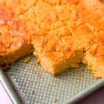 a close-up from the corner of a rectangular tray of freshly baked homemade sweet cornbread, with three portions cut out
