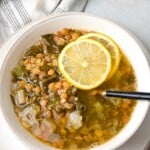 a top view of a bowl of lentil and Swiss chard soup served with lemon wedges on top