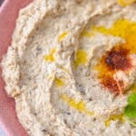 A close up image of baba ghanouj drizzled with olive oil and garnished with lemon slice