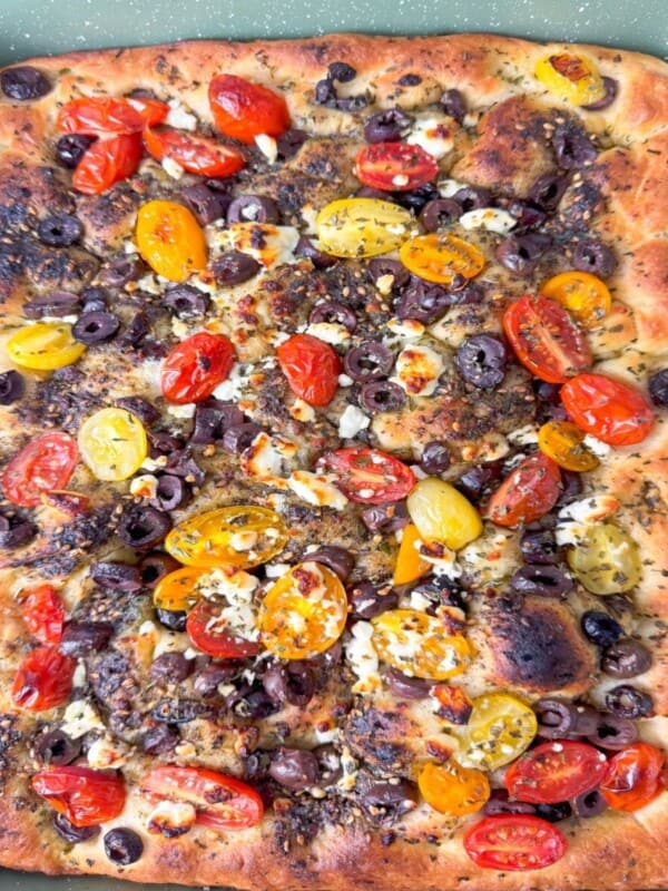Freshly baked zaatar focaccia in a rectangular pan, with crispy edges, airy bubbles, and vibrant Mediterranean toppings.