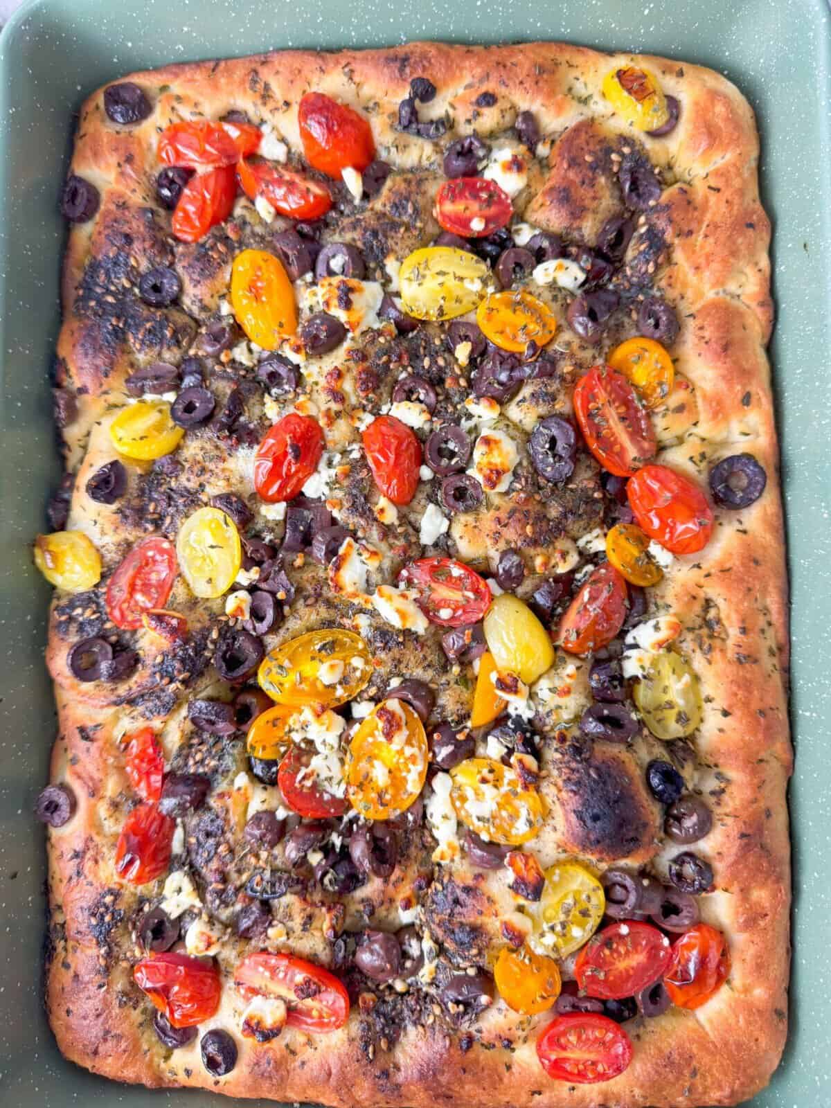 Zaatar Focaccia Freshly baked zaatar focaccia in a rectangular pan, with crispy edges, airy bubbles, and vibrant Mediterranean toppings.