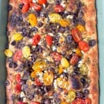 Freshly baked zaatar focaccia in a rectangular pan, with crispy edges, airy bubbles, and vibrant Mediterranean toppings.
