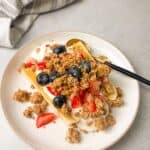 A beautifully plated Greek Yogurt Banana Split with fresh berries and granola on a white plate.