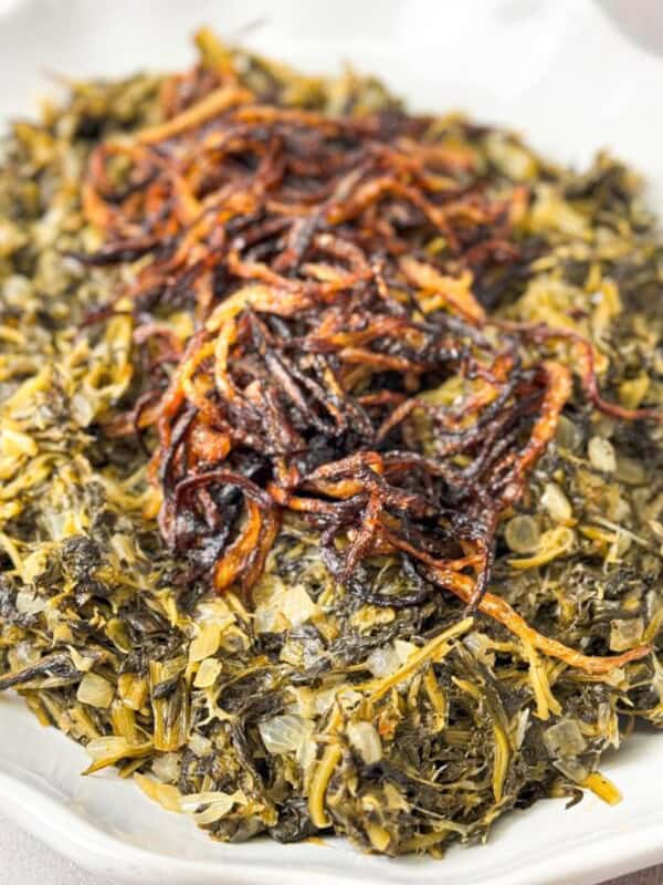 Close-up of Lebanese dandelion greens salad, topped with caramelized onions, and served on a white plate.