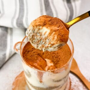 close-up of a spoon scooping creamy tiramisu chia seed pudding from a glass cup, revealing its rich layers of soaked chia seeds, coffee-infused flavor, and a dusting of cocoa powder on top