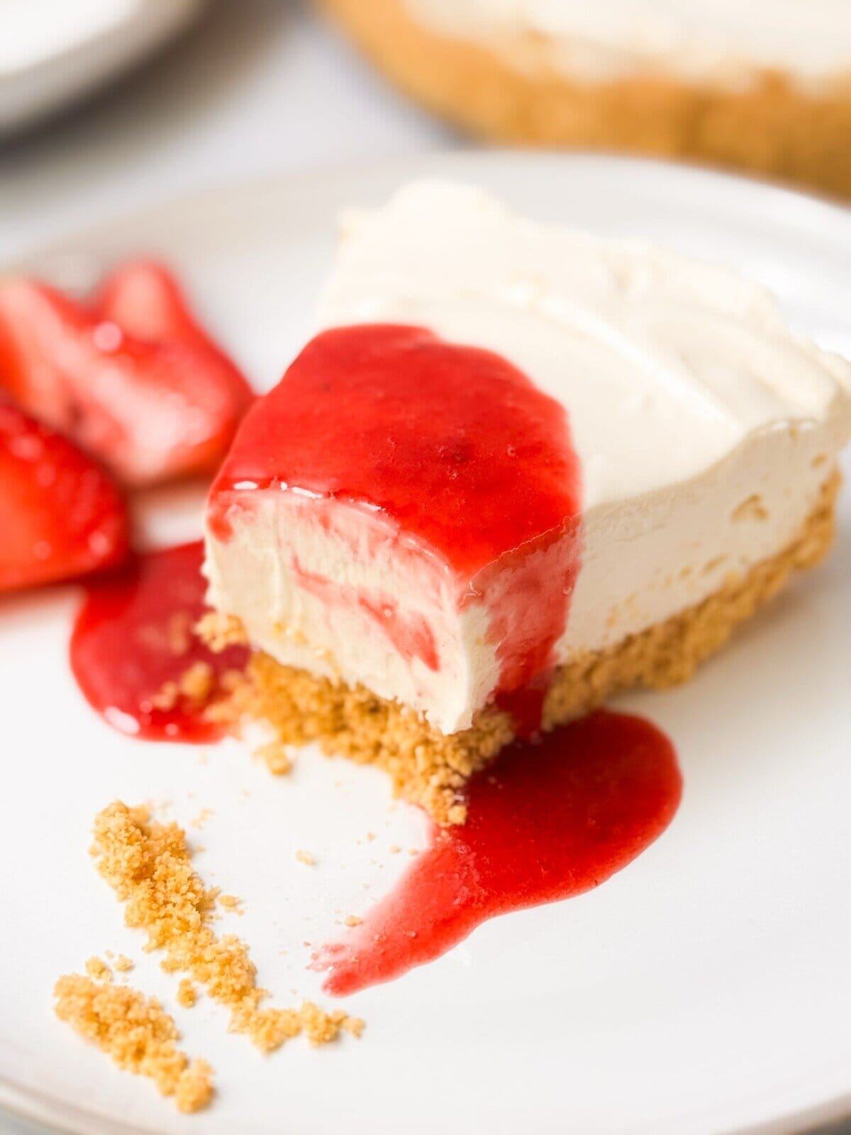 Best No-Bake Cheesecake a close shot of a slice of no-bake cheesecake drizzled with strawberry sauce on top, served on a plate
