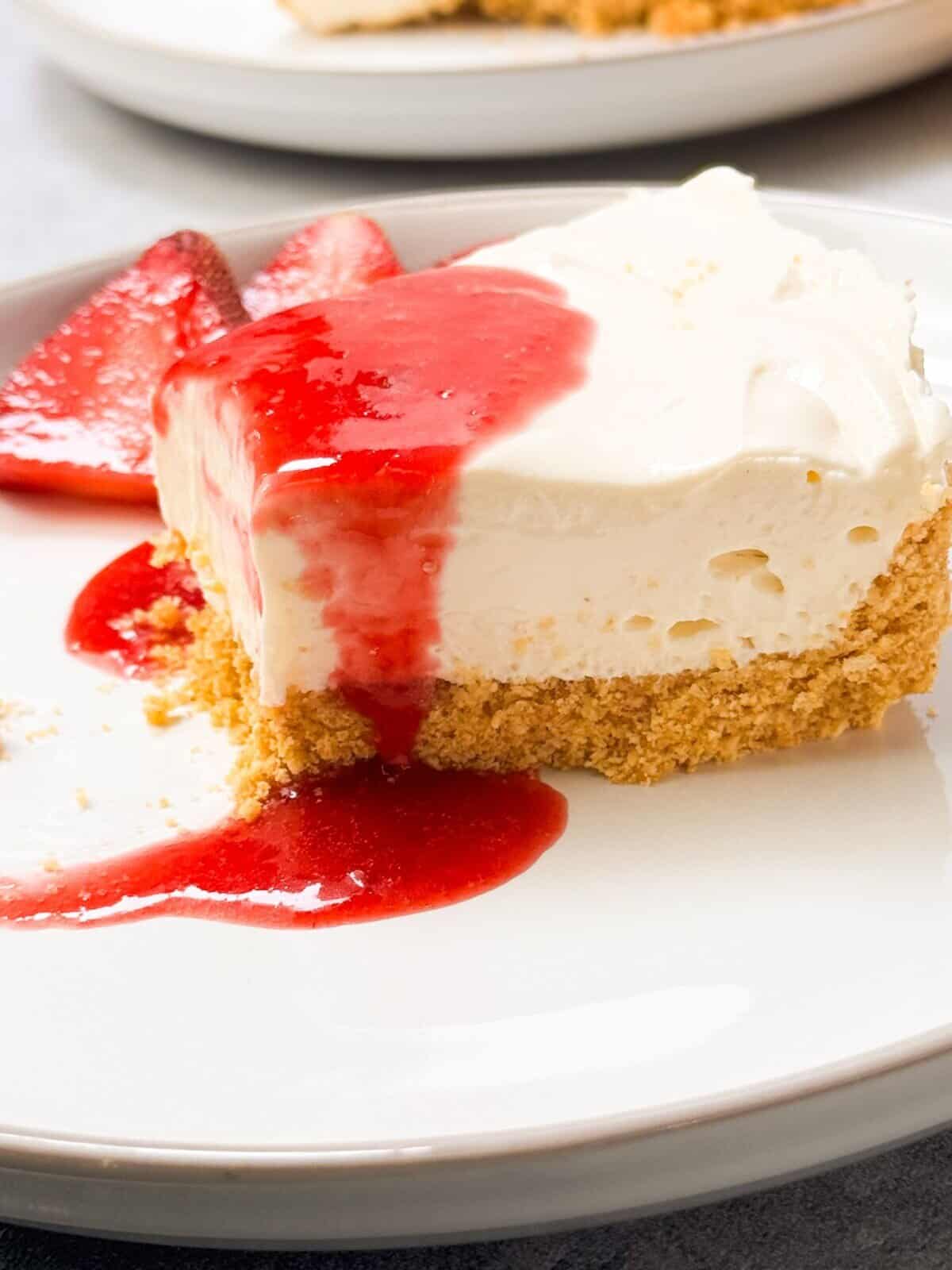 a side shot of a slice of no-bake cheesecake drizzled with strawberry sauce on top, served on a plate