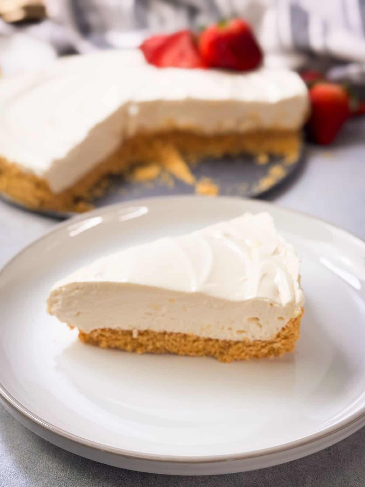 a slice of no-bake cheesecake served on a plate next to no-bake cheesecake with two slices out