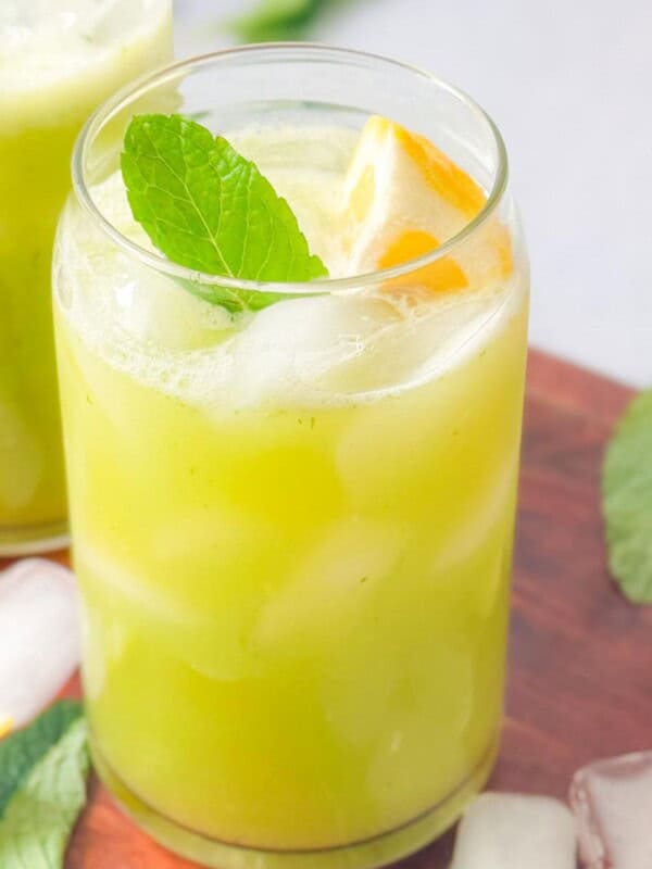 two cups of mint lemonade with lemon and mint garnish served on a wooden platter with ice, mint, an lemon wedges
