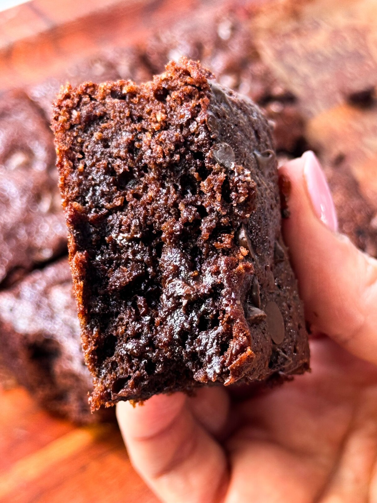 Fudgy Almond Flour Brownies A woman holding a fudgy gluten-free brownie with melted chocolate chips in her hands.