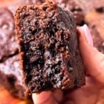 A woman holding a fudgy gluten-free brownie with melted chocolate chips in her hands.