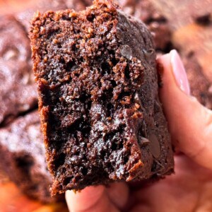 A woman holding a fudgy gluten-free brownie with melted chocolate chips in her hands.