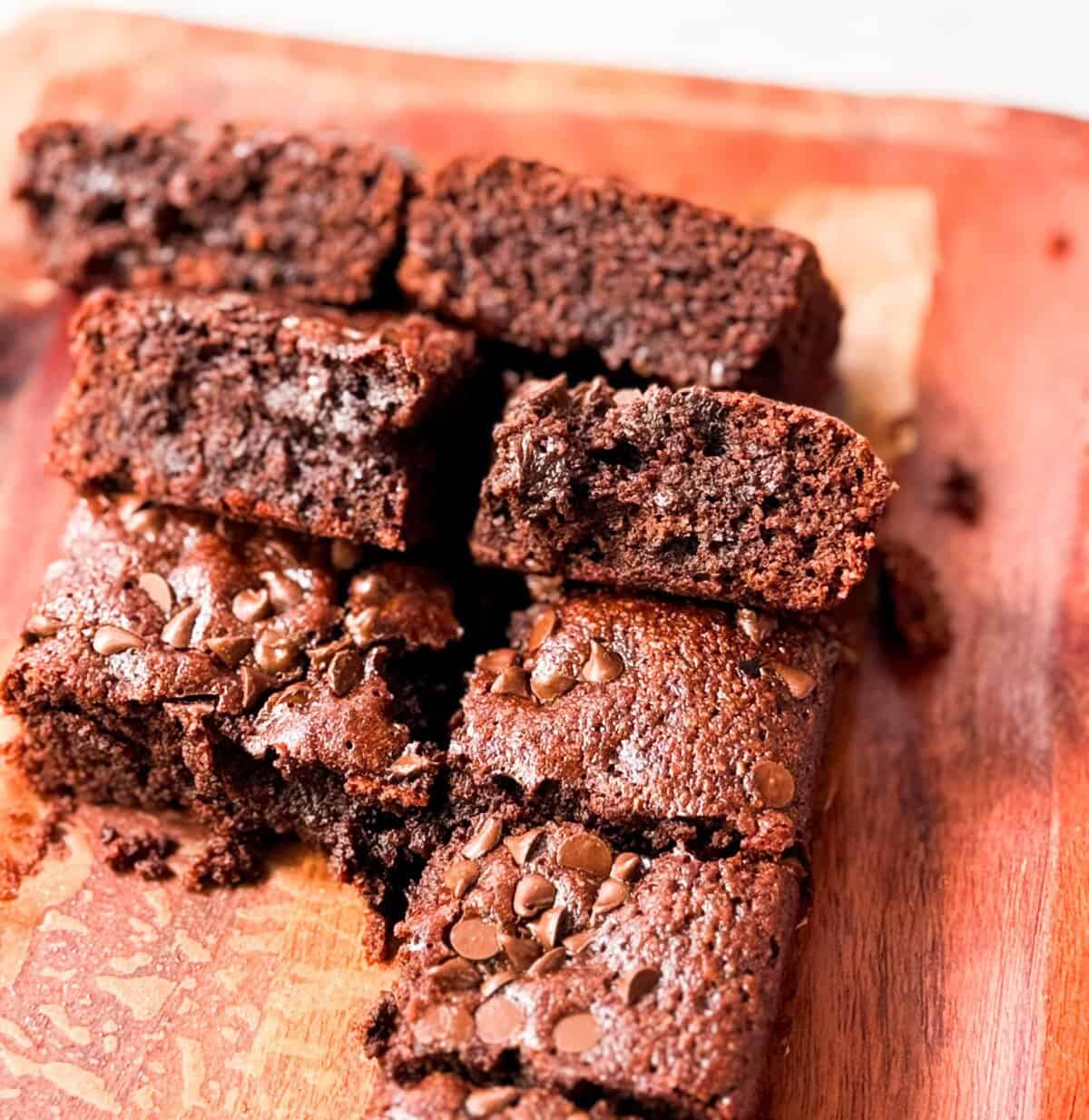 A stack of rich, fudgy almond flour brownies on a parchment paper, topped with extra chocolate chips.
