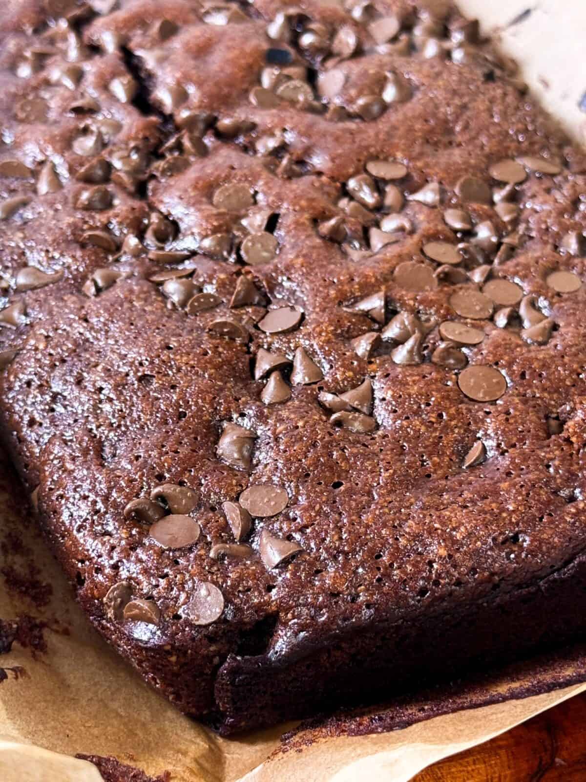 Freshly baked gluten-free brownies on parchment-paper, ready to be sliced.