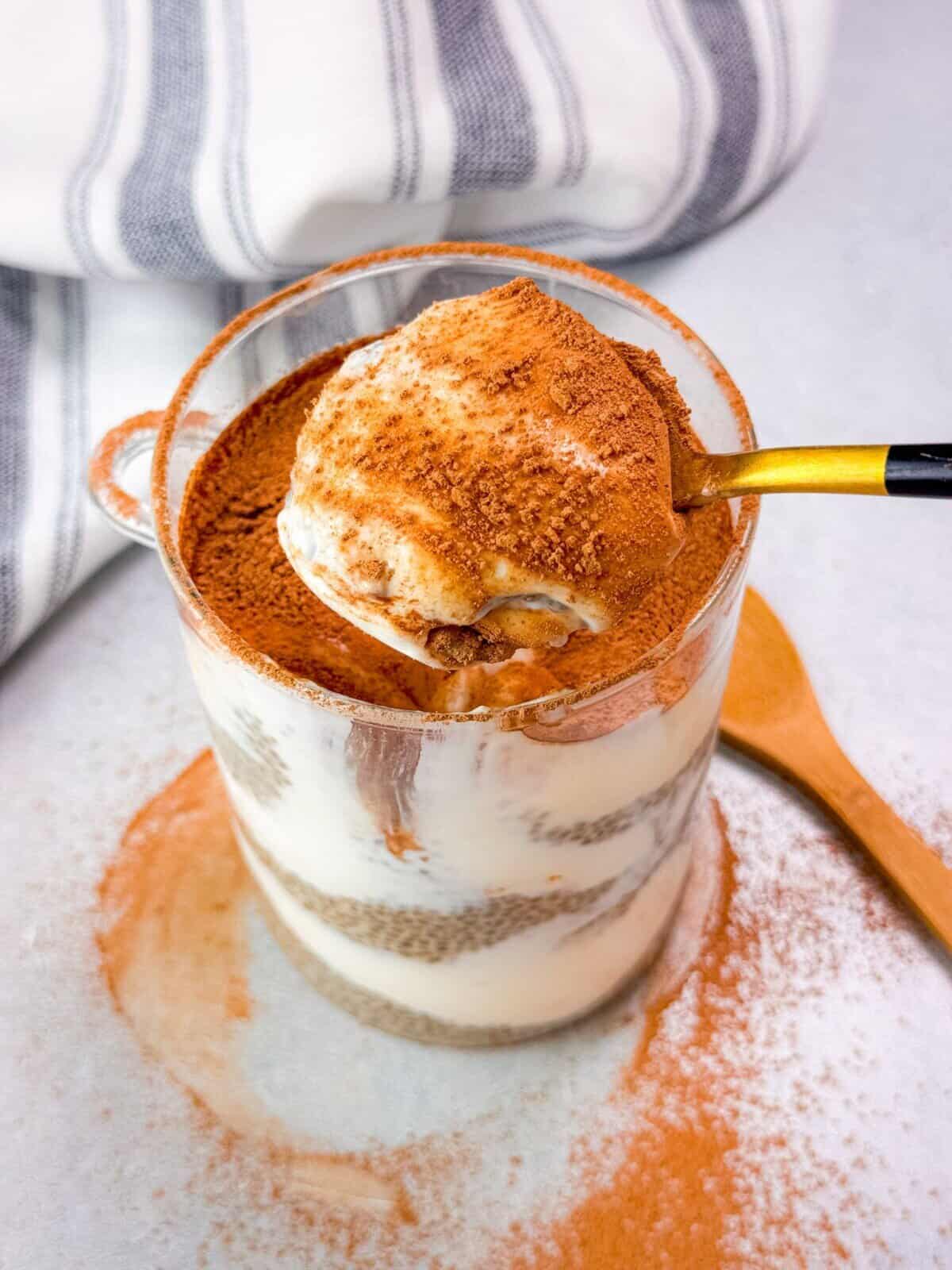 tiramisu chia pudding in a glass cup with a spoon lifting a portion to showcase its creamy layers and 