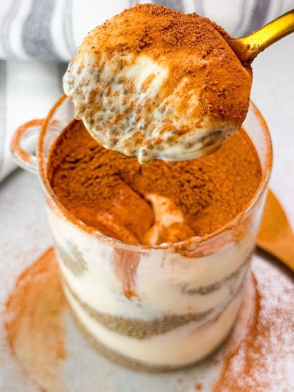 close-up of a spoon scooping creamy tiramisu chia seed pudding from a glass cup, revealing its rich layers of soaked chia seeds, coffee-infused flavor, and a dusting of cocoa powder on top