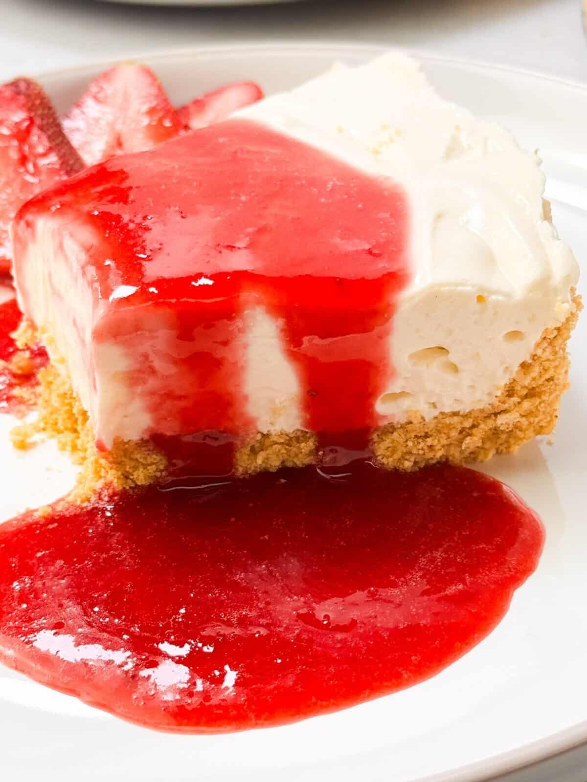 a side shot of a slice of no bake cheesecake drizzled with strawberry rosemary sauce on top