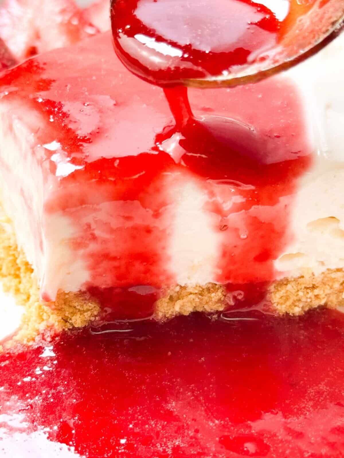 a close shot of drizzling a spoonful of strawberry rosemary sauce over a slice of no bake cheesecake