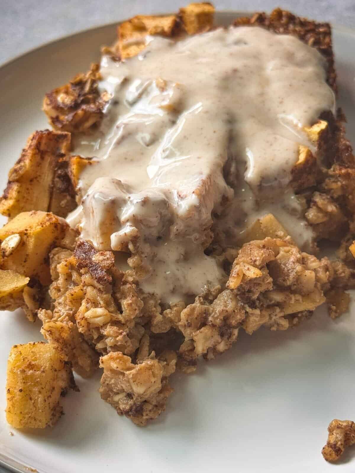 Apple Cinnamon Oatmeal Bake close up of a piece of cinnamon apple baked oatmeal served in a white plate topped with yogurt frosting