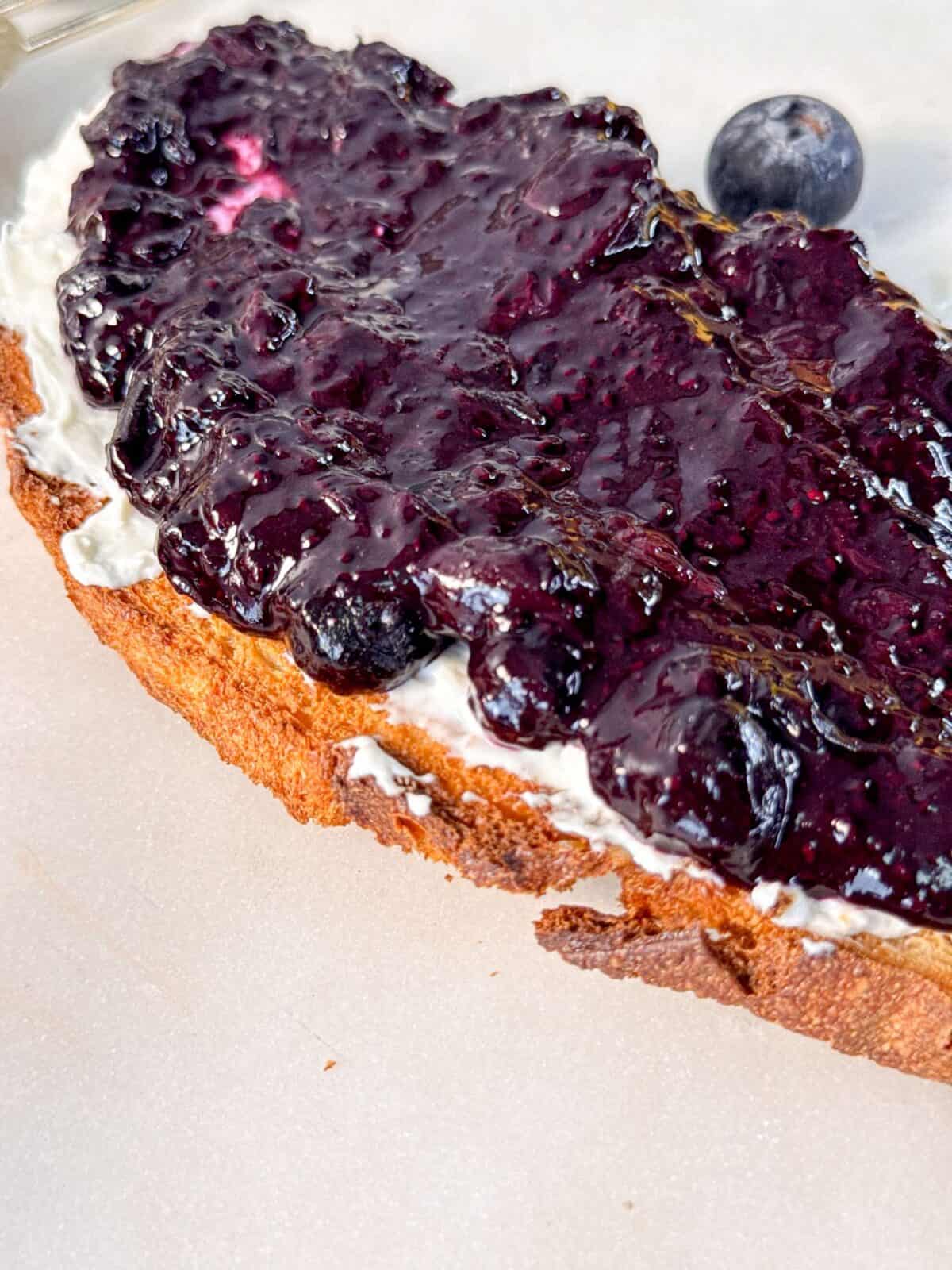 2 Ingredient Blueberry Chia Jam a close up shot of a slice of bread topped with cream cheese and blueberry chia jam.