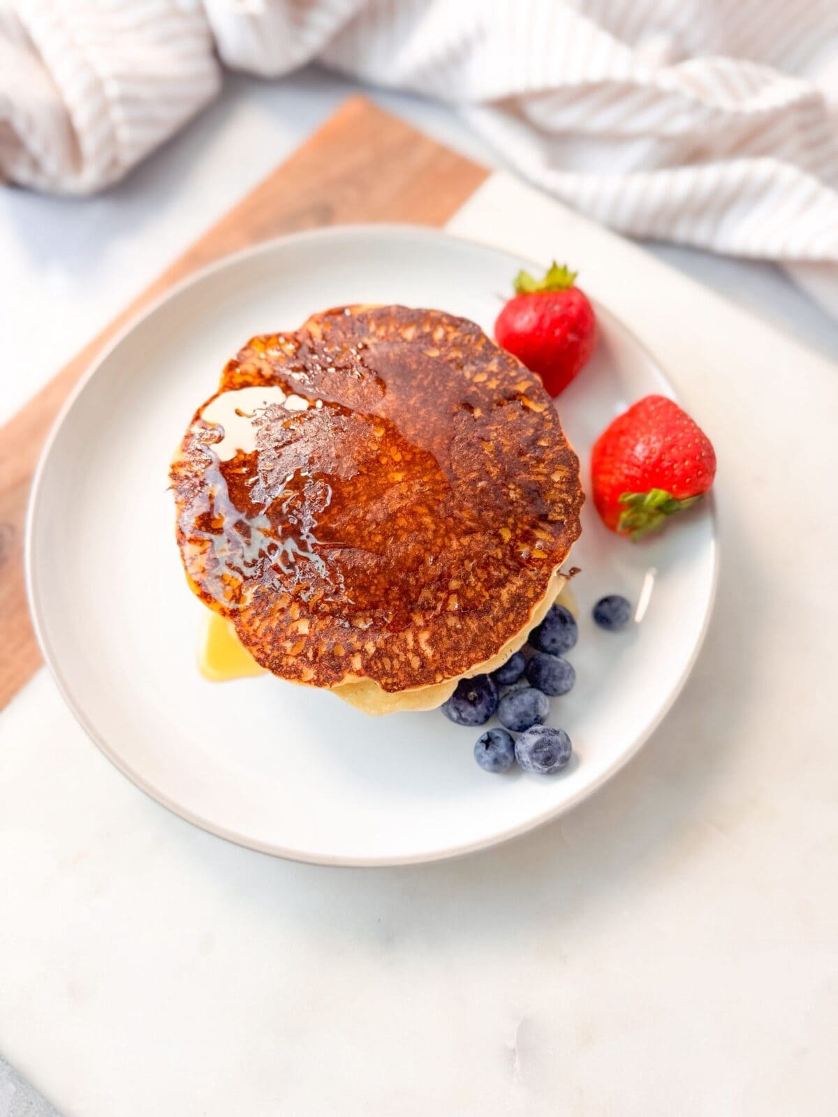 Almond Flour Cottage Cheese Pancakes A top shot of a stack of almond flour cottage cheese pancakes topped with syrup, served with fresh strawberries and blueberries on a white plate.