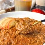 Close-up of apple cinnamon steel cut oats in a bowl, topped with apple slices and cinnamon, with a spoonful lifted.
