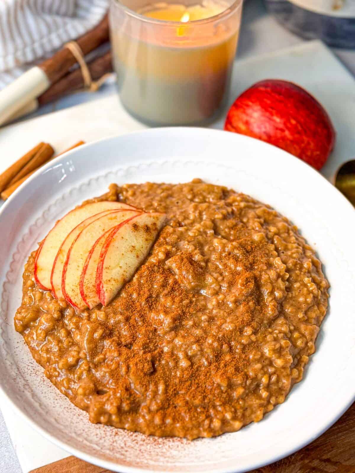 Apple Cinnamon Steel Cut Oats Recipe A bowl of apple cinnamon steel cut oats topped with sliced apples and cinnamon, with a candle and apple in the background.