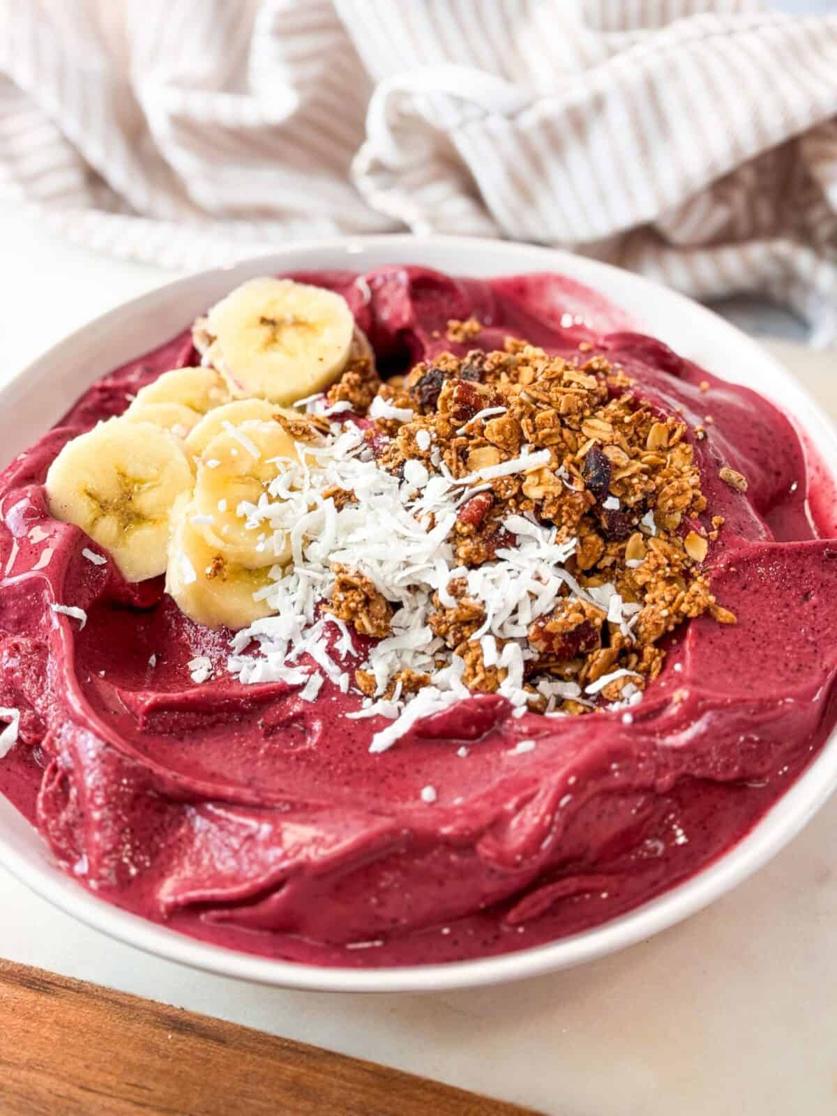 Berry Smoothie Bowl Thick and creamy berry smoothie bowl topped with sliced banana, granola, and shredded coconut in a white bowl