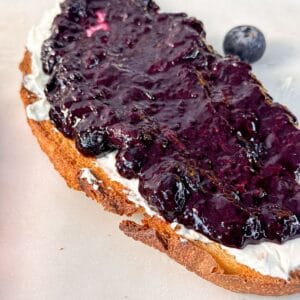 A slice of toasted bread spread with cream cheese and topped with thick blueberry chia jam.