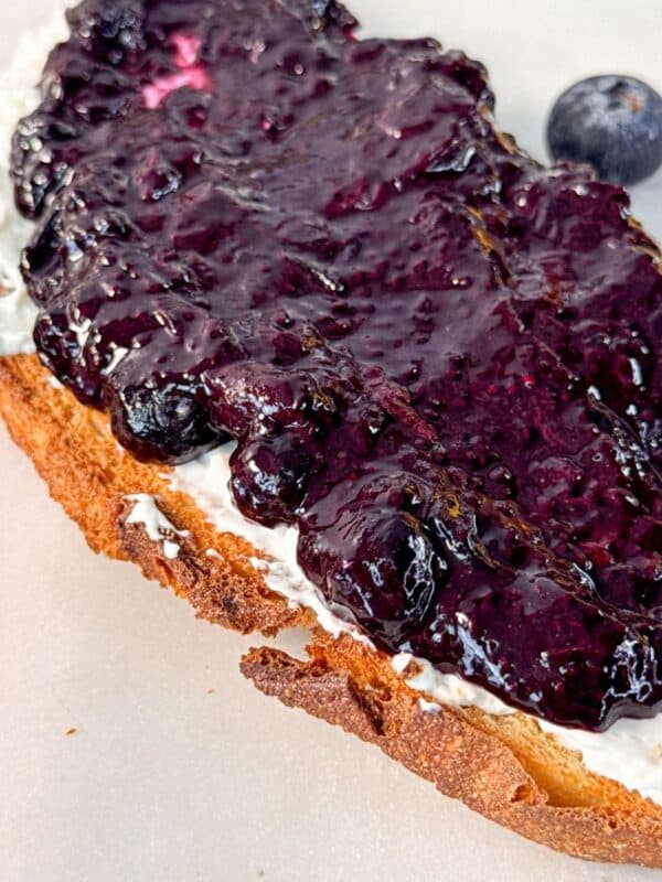 A slice of toasted bread spread with cream cheese and topped with thick blueberry chia jam.