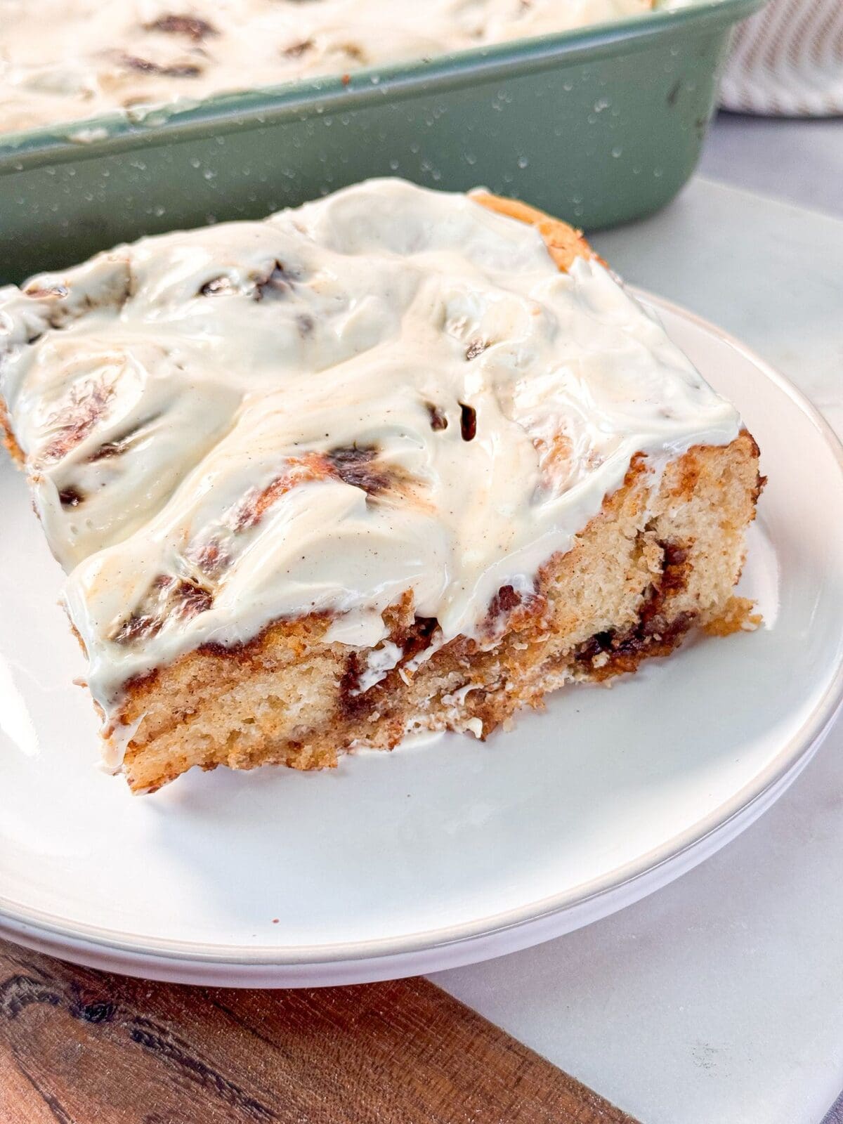 Cinnamon Roll Focaccia a shot of a slice of fluffy soft cinnamon roll focaccia topped with cream cheese icing