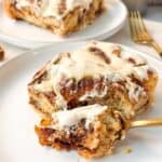 a close shot of a plate of a slice of fluffy soft cinnamon roll focaccia topped with cream cheese icing with one bite out