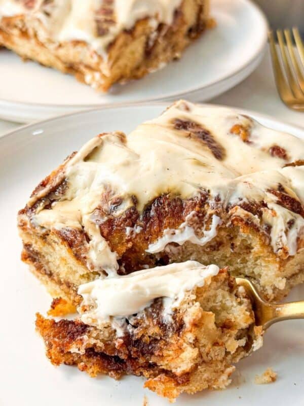 a close shot of a plate of a slice of fluffy soft cinnamon roll focaccia topped with cream cheese icing with one bite out
