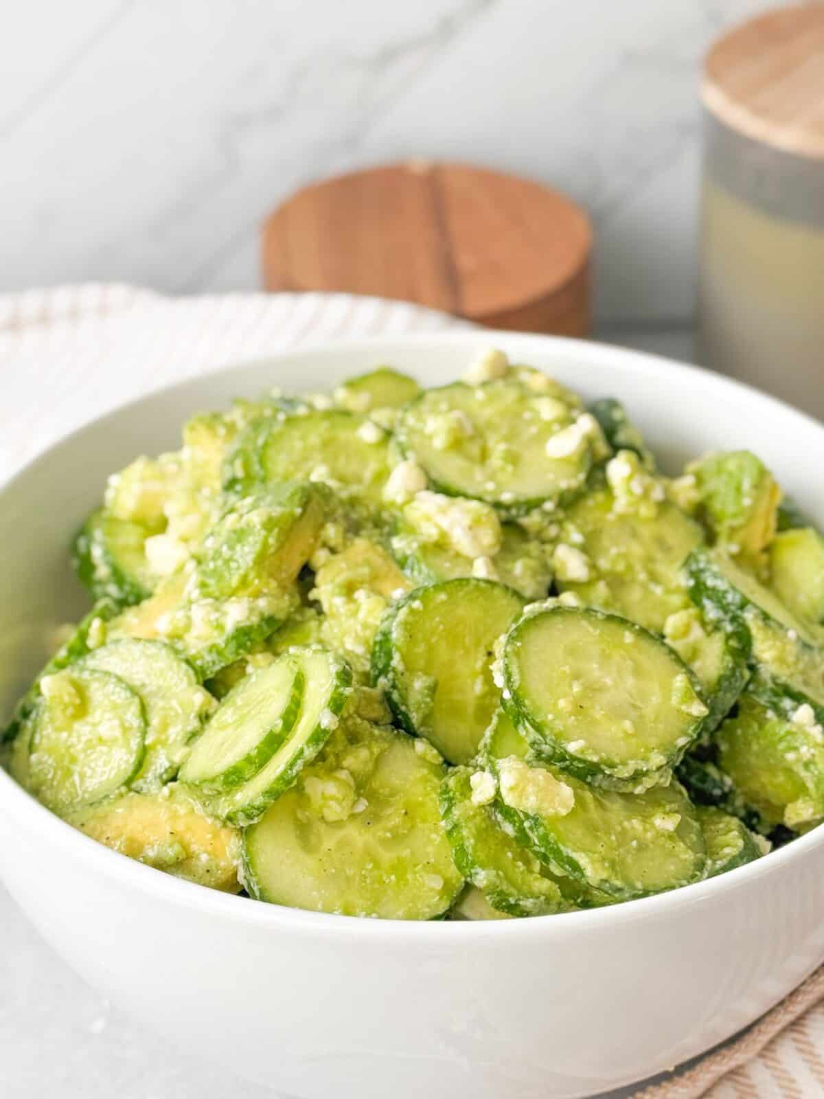 Creamy Cucumber Feta Salad A shot of creamy cucumber feta salad served in a white bowl. The salad features sliced cucumbers mixed with creamy avocado chunks and crumbled feta cheese.