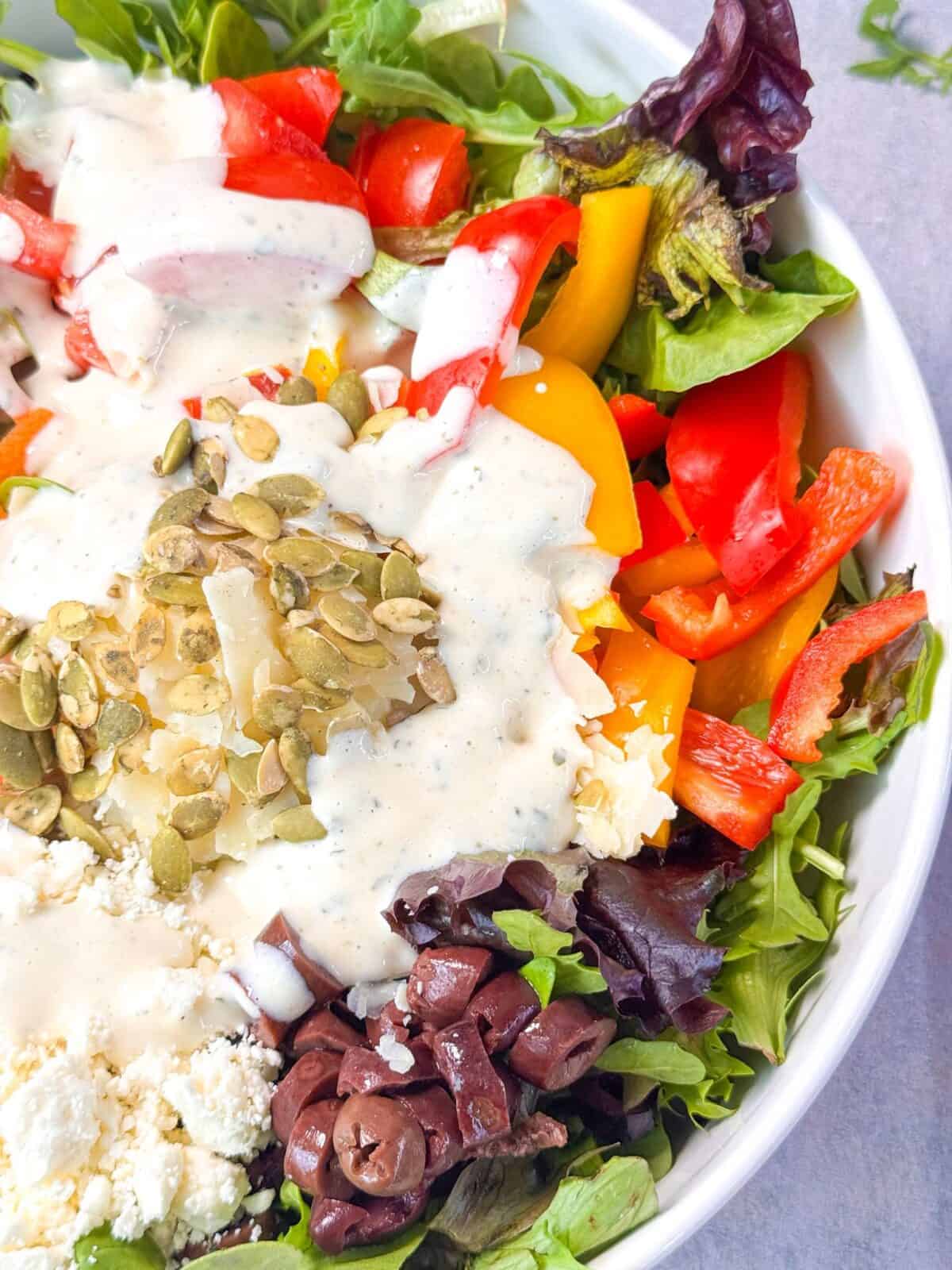 Creamy Homemade Ranch Dressing a top shot of fresh salad bowl made with arugula, shredded carrots, bell peppers, feta, olives, pumpkin seeds, and topped with ranch dressing