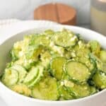 A close-up shot of fresh cucumber feta salad served in a white bowl.