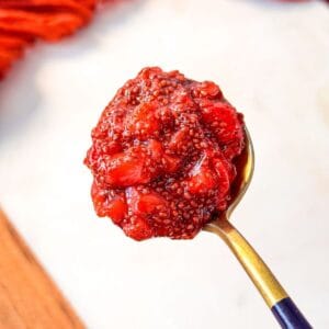 a close up shot of a spoonful of homemade strawberry chia jam with visible chia seeds and strawberry chunks.