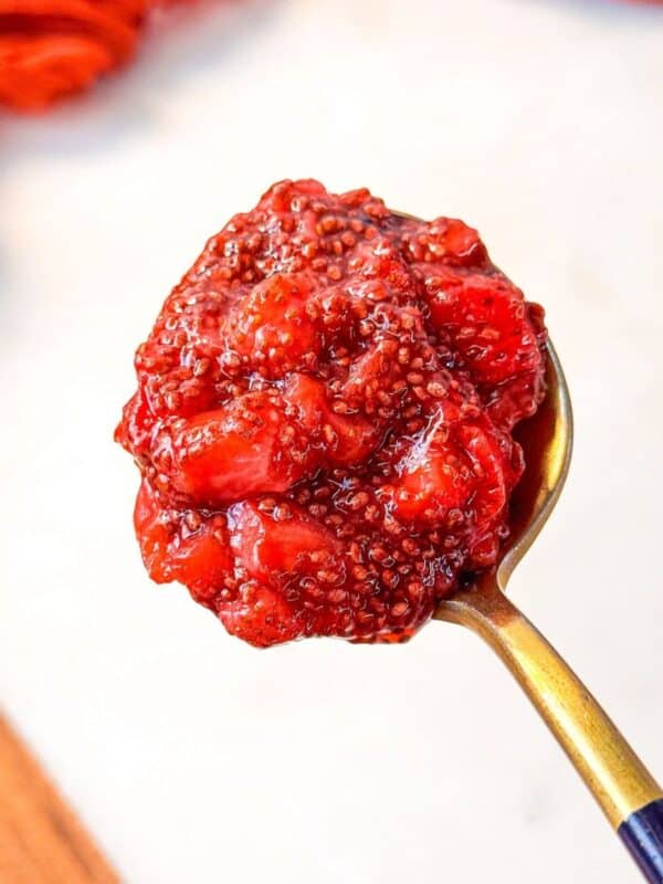 a close up shot of a spoonful of homemade strawberry chia jam with visible chia seeds and strawberry chunks.