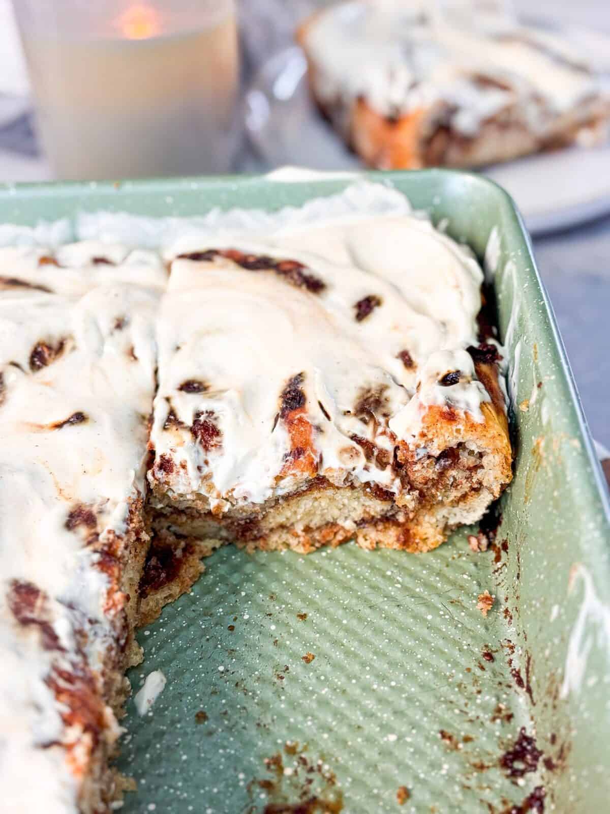 Fluffy Cinnamon Roll Focaccia a shot of a the baking pan of fluffy cinnamon roll focaccia topped with cream cheese icing with one slice out