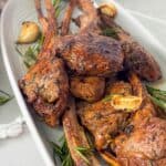 Perfectly cooked garlic rosemary lamb chops garnished with fresh rosemary and roasted garlic on a white platter
