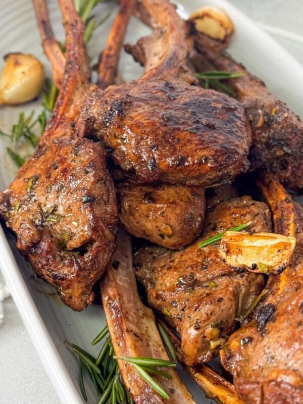 Perfectly cooked garlic rosemary lamb chops garnished with fresh rosemary and roasted garlic on a white platter
