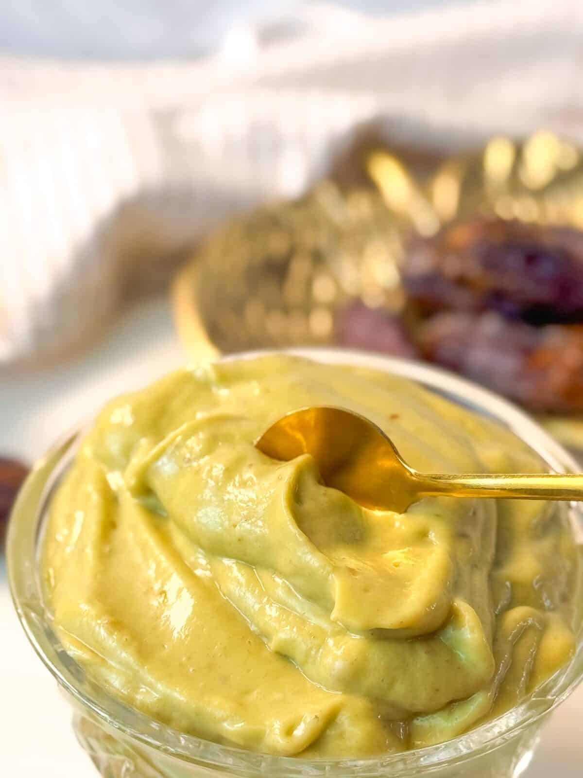 Healthy Avocado Date Pudding Close-up shot of a glass bowl filled with creamy avocado date pudding, with a golden spoon dipped inside.