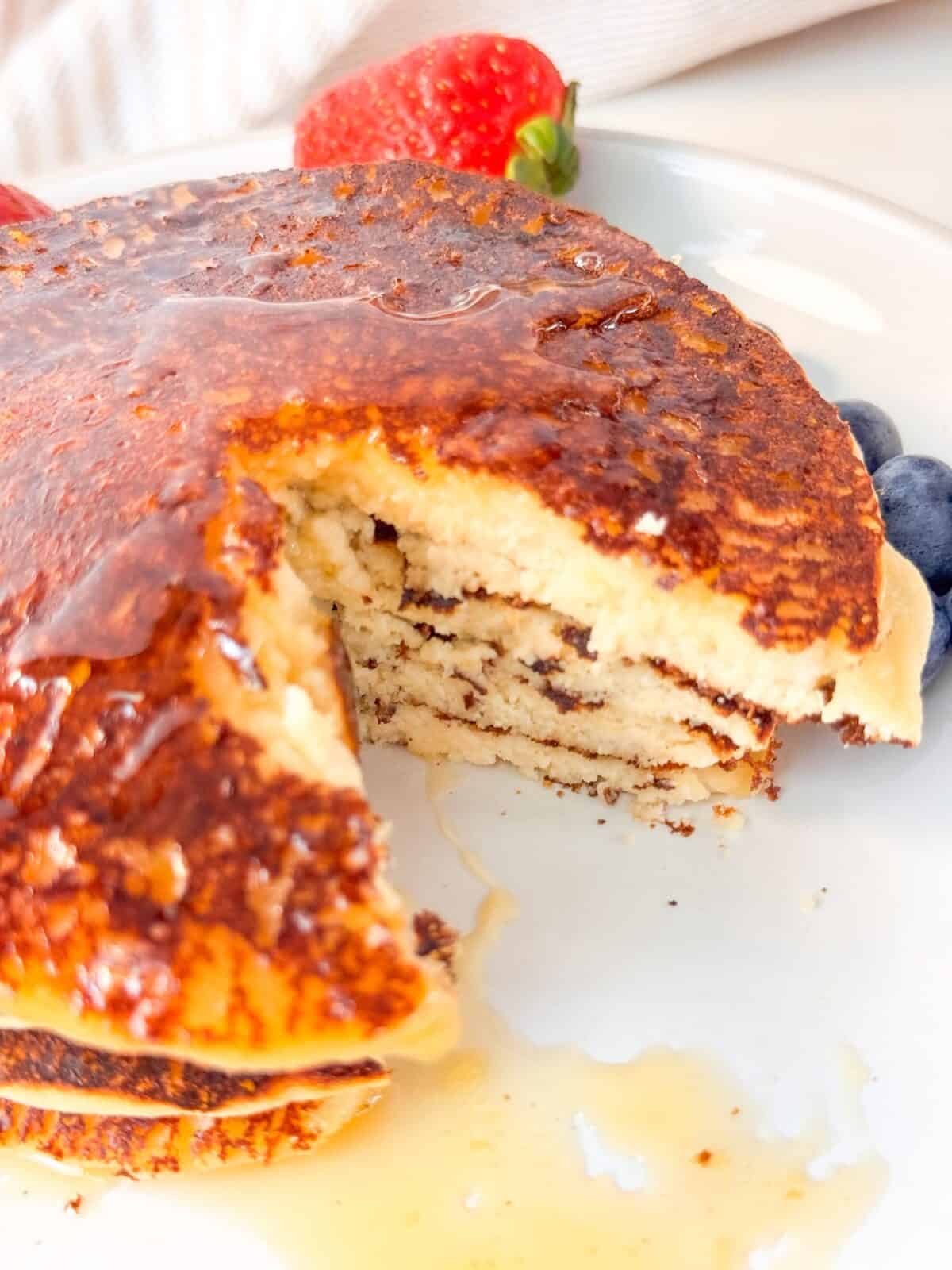 High Protein Cottage Cheese Almond Flour Pancakes Stack of cottage cheese almond flour pancakes cut open to show fluffy layers, drizzled with honey, and served with strawberries.