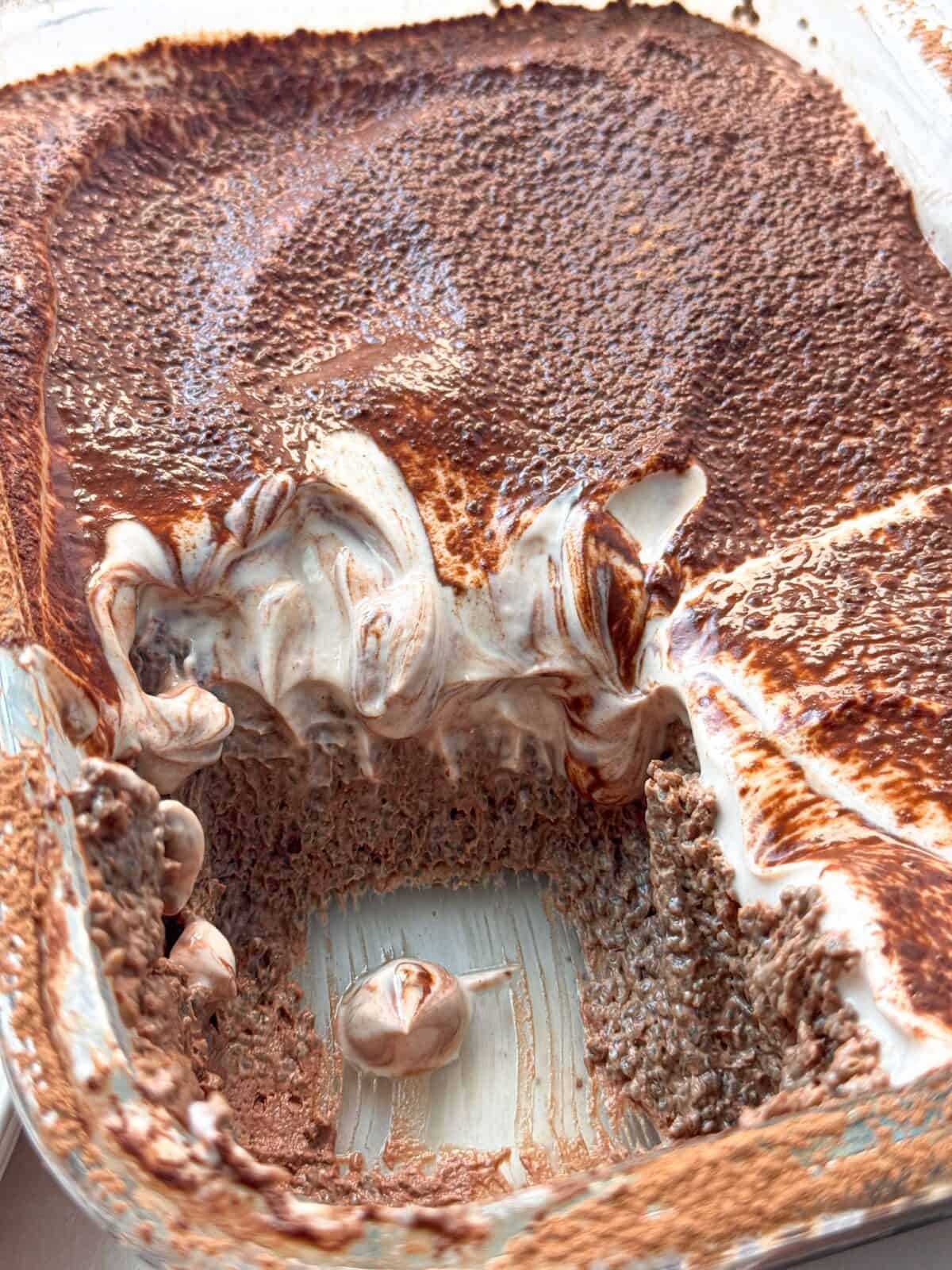 High Protein Mocha Chia Pudding Cake Pirex dish of high protein mocha chia pudding cake topped with whipped cream and cocoa powder, partially scooped out.