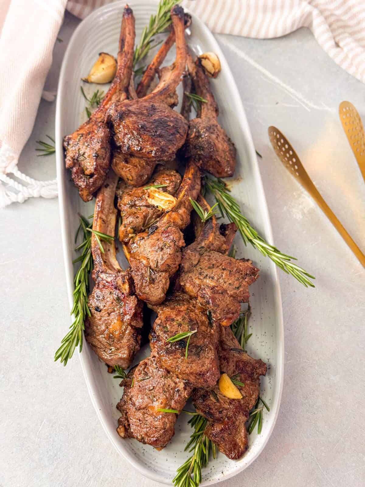 Tender Juicy Lamb Chops Recipe Plate of lamb chops cooked to perfection, garnished with fresh rosemary sprigs and roasted garlic cloves