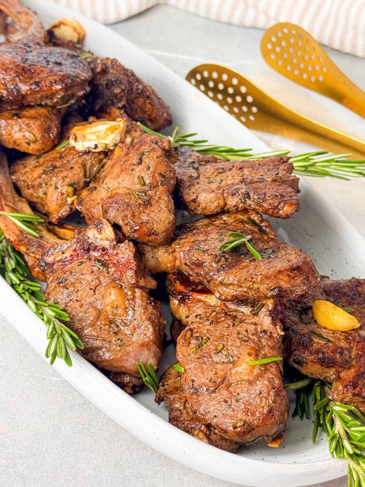 Lamb Chops with Rosemary and Garlic Delicious seared lamb chops stacked on a serving platter with fresh herbs and roasted garlic