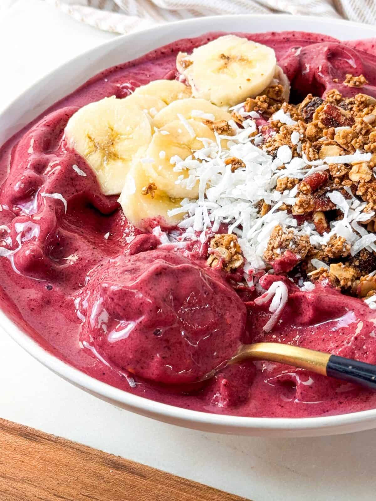 Mixed Berry Smoothie Bowl Spoonful of thick frozen berry smoothie bowl topped with banana slices, coconut, and granola