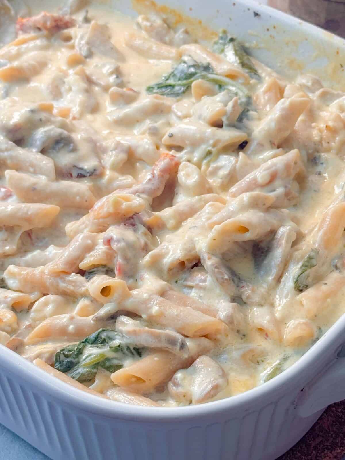 One-Pan Baked Creamy Boursin Pasta Close up shot of creamy pasta bake with penne, mushrooms, spinach, and sun-dried tomatoes stirred together.